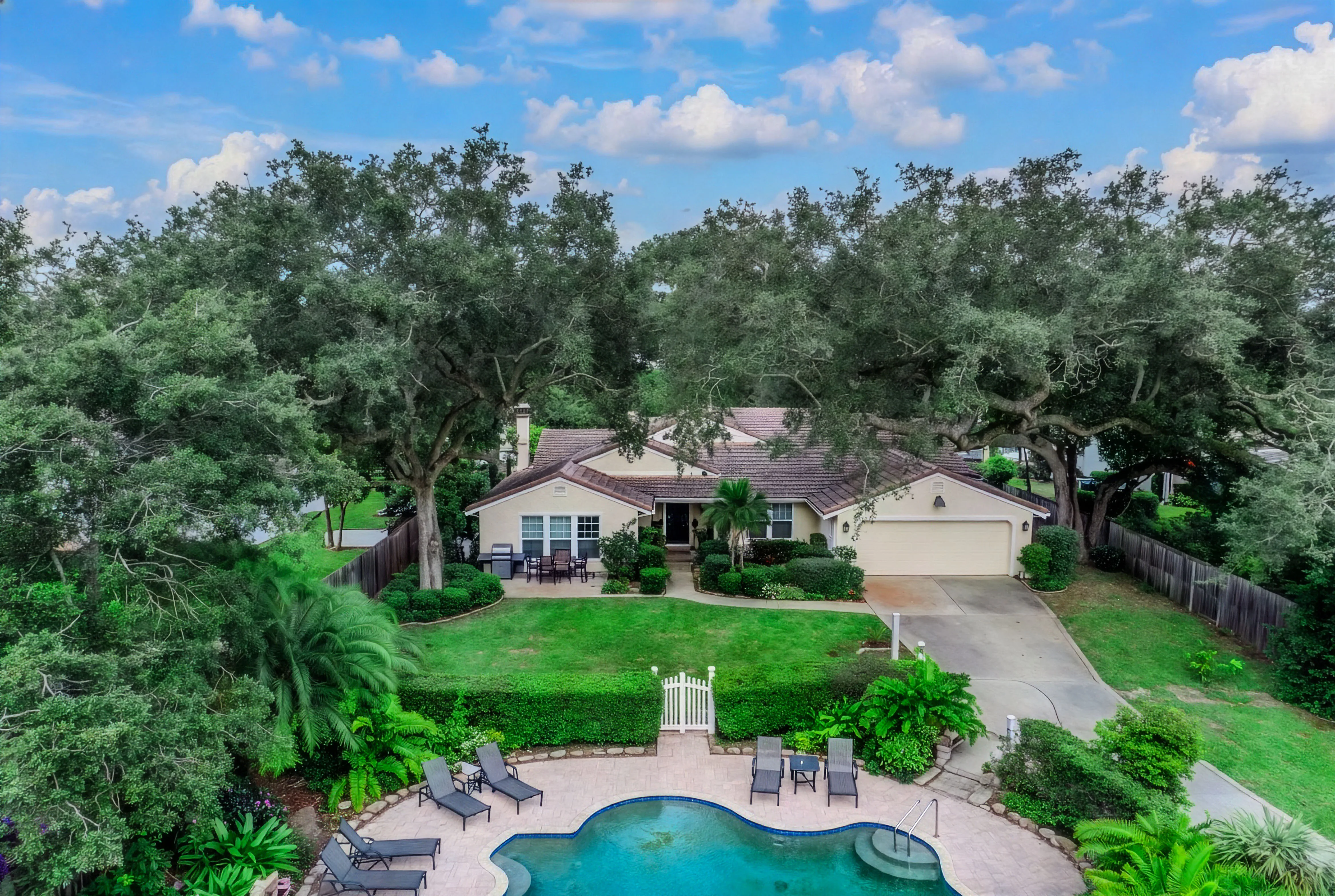 Aerial of a ranch home under an oak canopy with a pool and outdoor area
