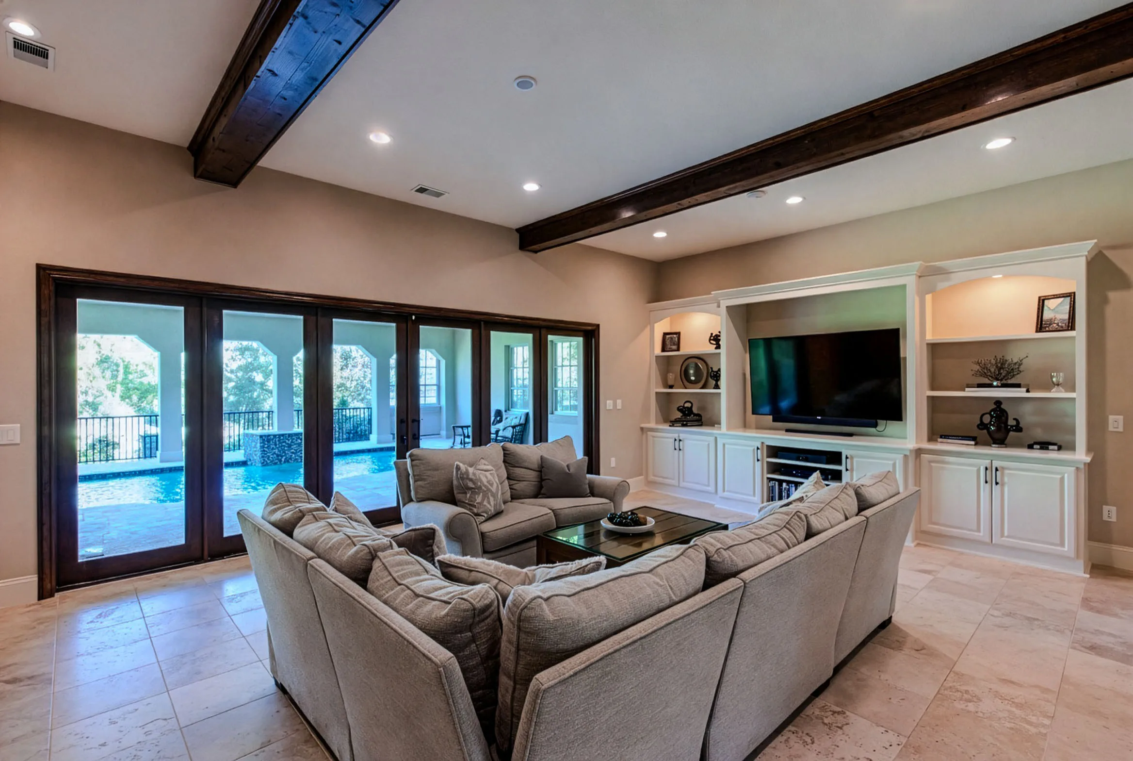 Great room with exposed wood beams, built-ins and French doors to the pool