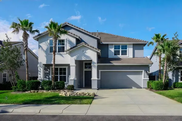 Two-story gray stucco home with palm trees, blue sky